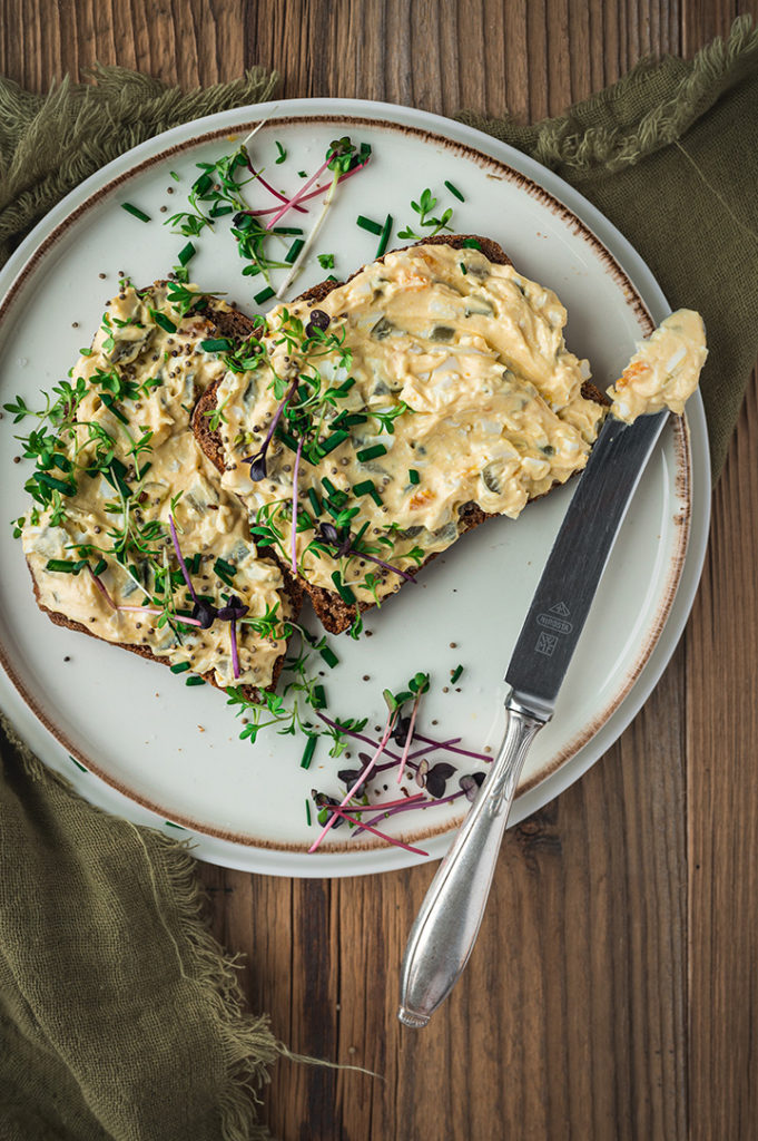 Ein Teller mit zwei Scheiben Roggenbrot belegt mit herzhaftem Eieraufstrich.