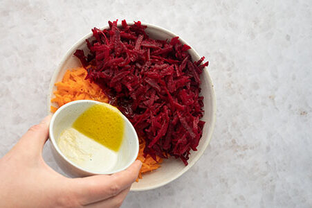 Eine Person gibt das Dressing über den Salat.