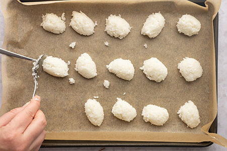 Eine Person formt mit zwei Löffeln die Makronen auf einem Backblech.