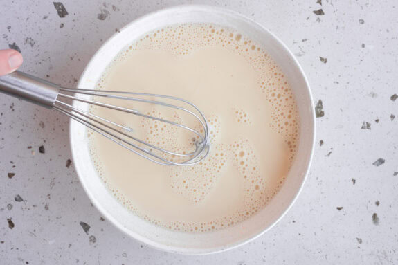 Eine Person rührt Milch in die Puddingpulver-Masse.