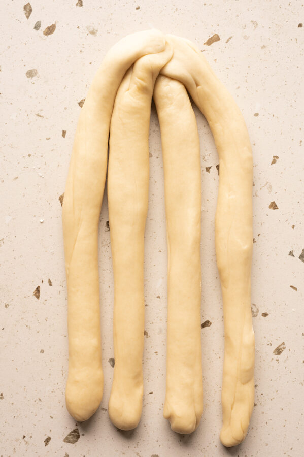 4 Teigstränge liegen nebeneinander und die Enden auf einer Seite sind zusammen gedrückt.