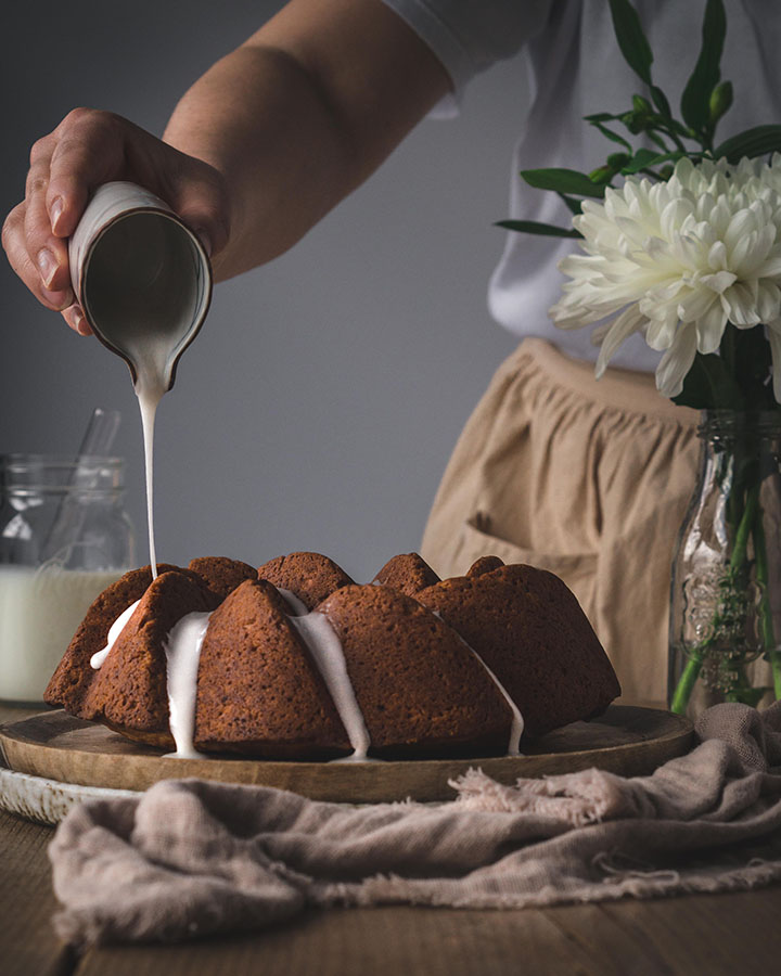 Eine Frau verteilt Zuckerguss über dem Zitronen-Buttermilch-Gugelhupf.