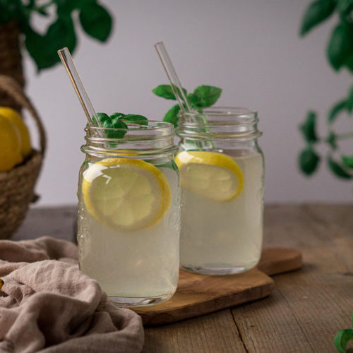 Basilikum-Zitronen-Limonade in Gläsern mit Glas-Strohhalmen auf einem Tisch