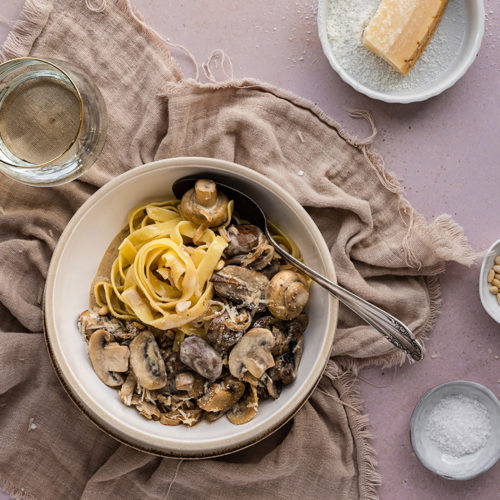 Ein Teller voll Pasta mit Champignons in Sahnesauce steht auf einem Tisch.