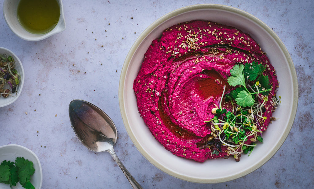 Eine Schüssel mit pinkfarbenem Rote Bete Humus steht auf einem Tisch.