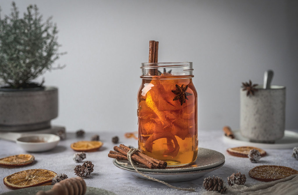 Ein Glas mit winterlichem Orangensirup aus Orangenschalen steht auf einem Tisch.