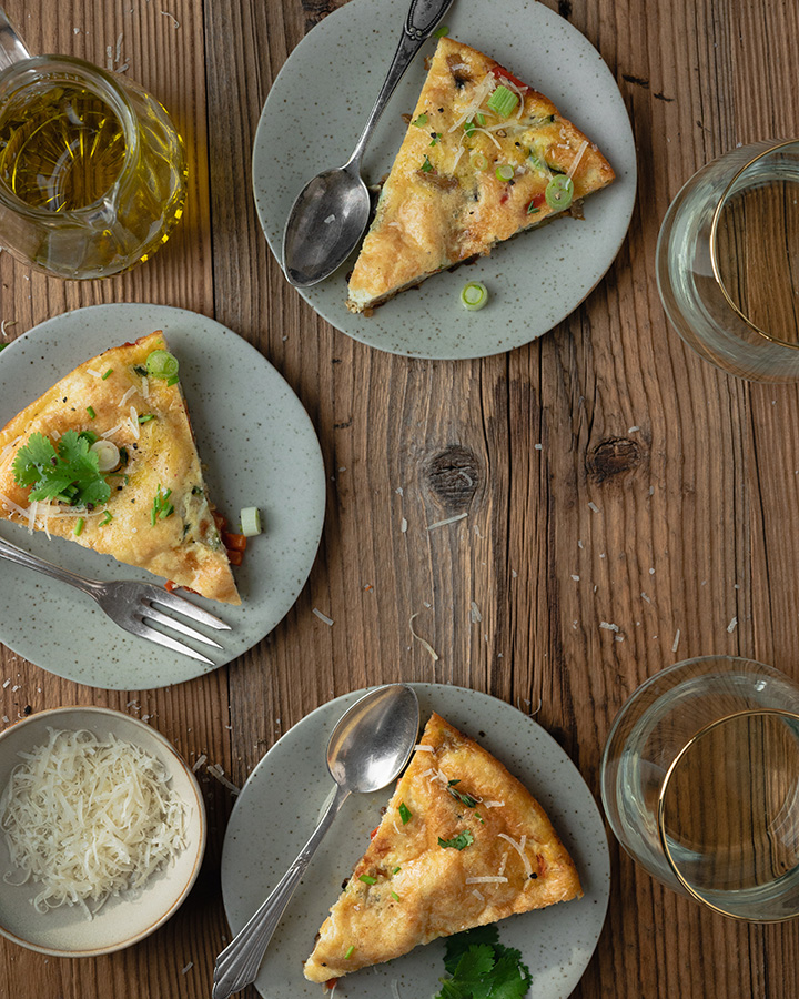 Drei Teller mit jeweils einem Stück Frittata stehen auf einem Tisch.