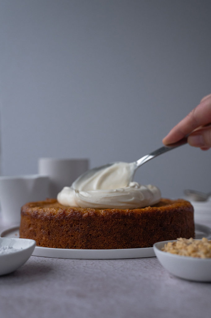 Eine Person verstreicht weißes Frischkäse-Frostiing auf dem Karottenkuchen.