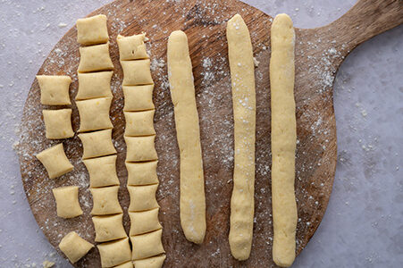 Der Gnocchi-Teig wurde in gleichlange "Würste" gerollt, die auf einem Brett liegen.