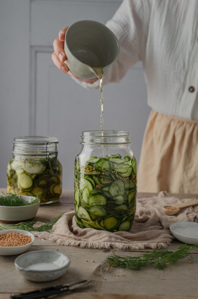 Eine Frau gießt heißen Sud über die Gurkenscheiben.