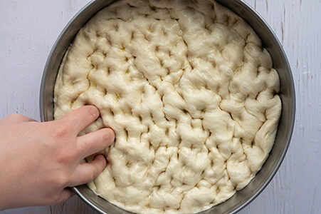 Eine Person drückt mit den Fingern Mulden in den Focaccia Teig