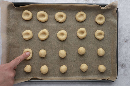 Eine Person drückt Mulden mit dem Finger in die Kekse.