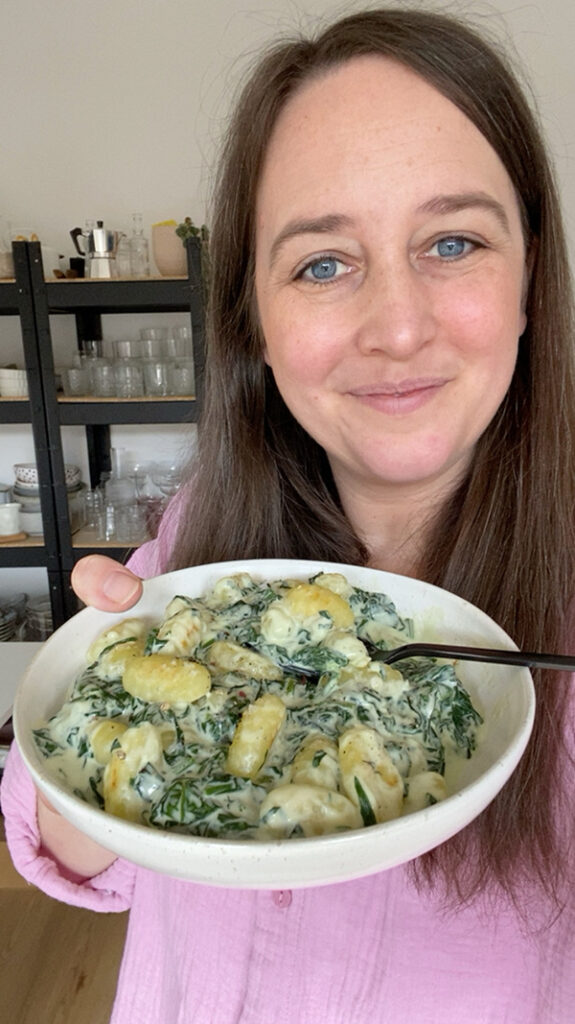 Eine Frau hält eine Schüssel mit Gnocchi in Spinat und Sahnesauce in der Hand.