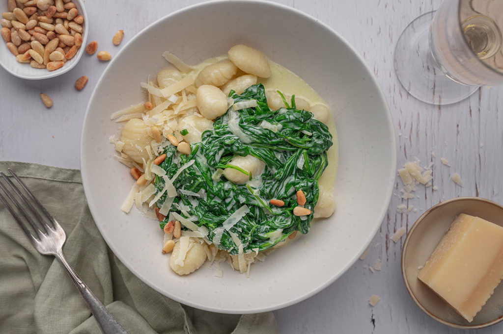 Ein Teller mit Gnocchi in Spinat-Sahnesauce steht auf einem Tisch.
