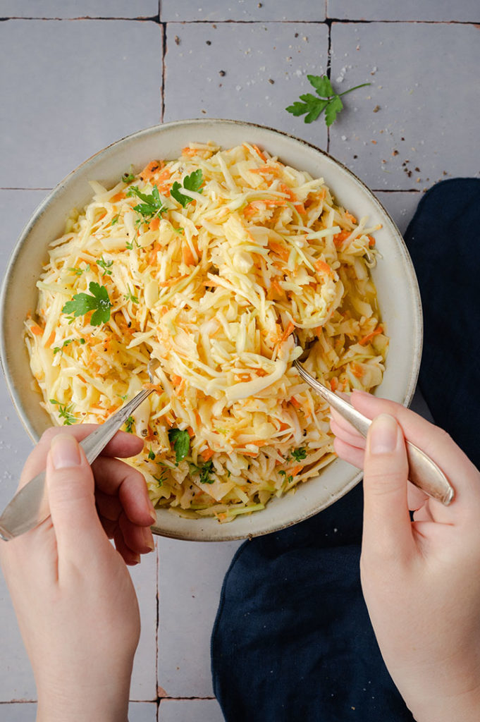 Eine Person verteilt den Coleslaw auf Teller.