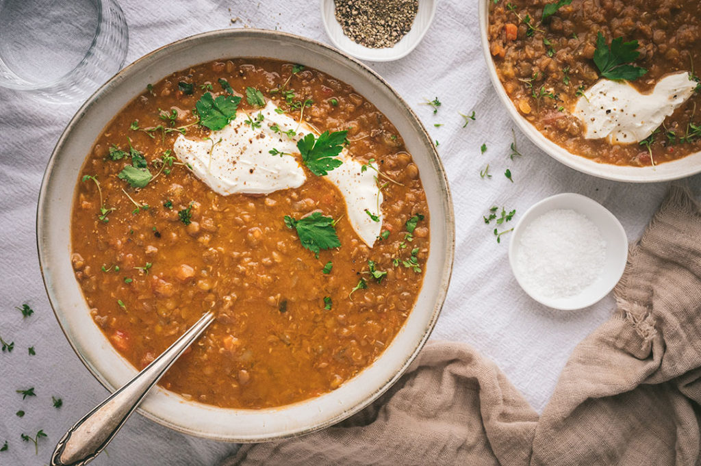 Ein großer Teller mit vegetarischer Linsensuppe steht auf einem Tisch.