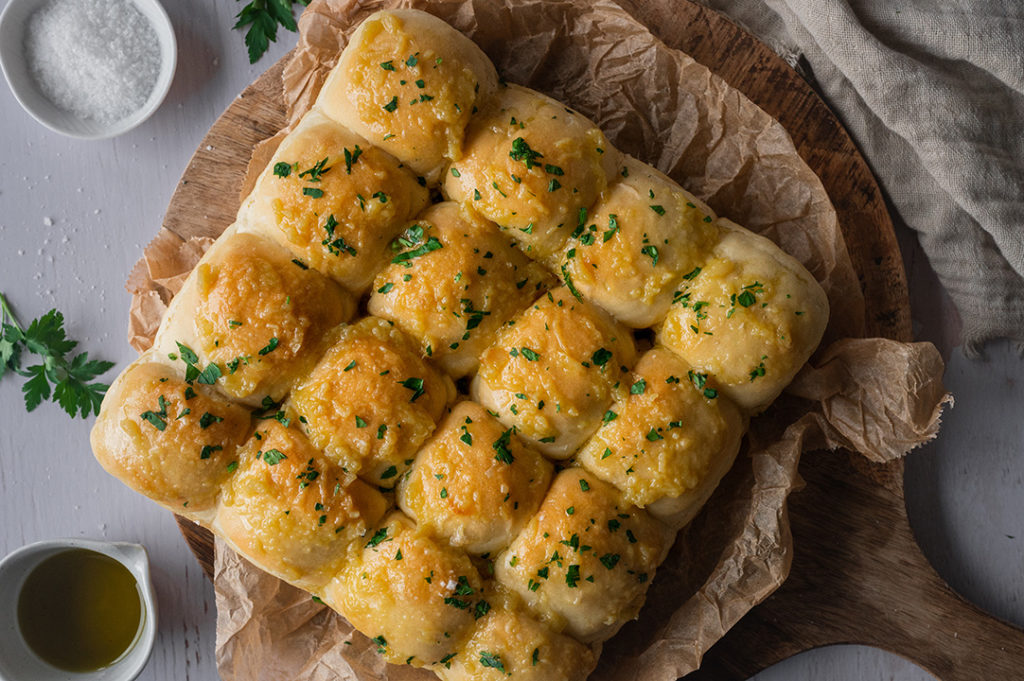 Die fertigen Knoblauch Brötchen liegen auf einem Brettchen.