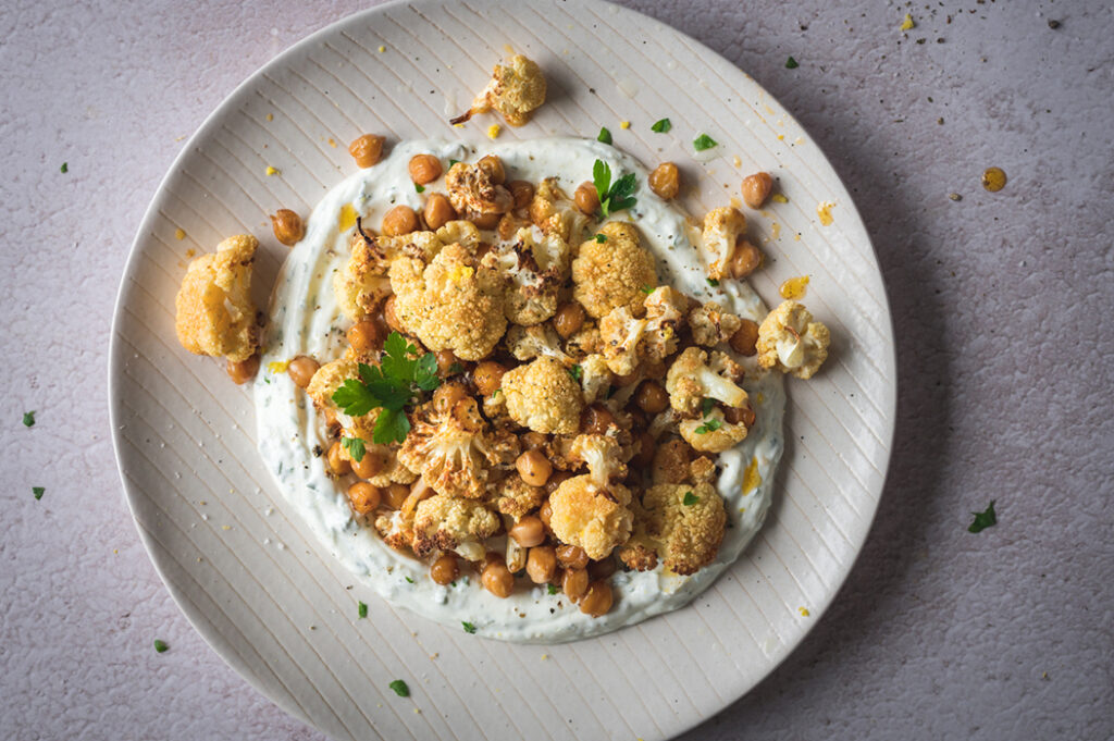 Ein großer Teller mit geröstetem Blumenkohl auf Joghurt Dip steht auf dem Tisch.