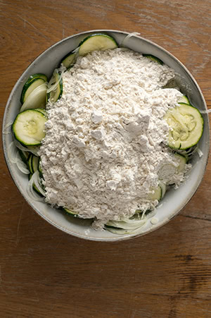 Die Mehl-Parmesan Mischung wird zu den Zucchini gegeben.