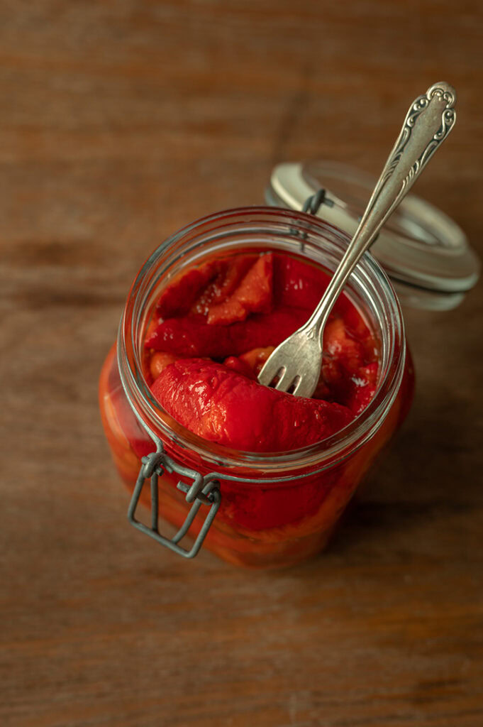 Ein Einmachglas mit eingelegter Paprika steht auf dem Tisch.