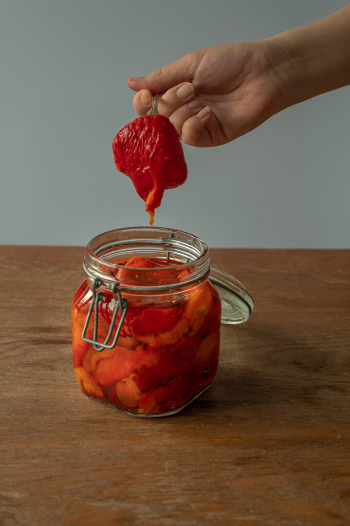 Eine Person nimmt eine eingelegte Paprika aus dem Glas.