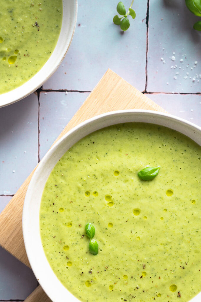 Zwei Teller mit Zucchini Suppe stehen auf einem Tisch.