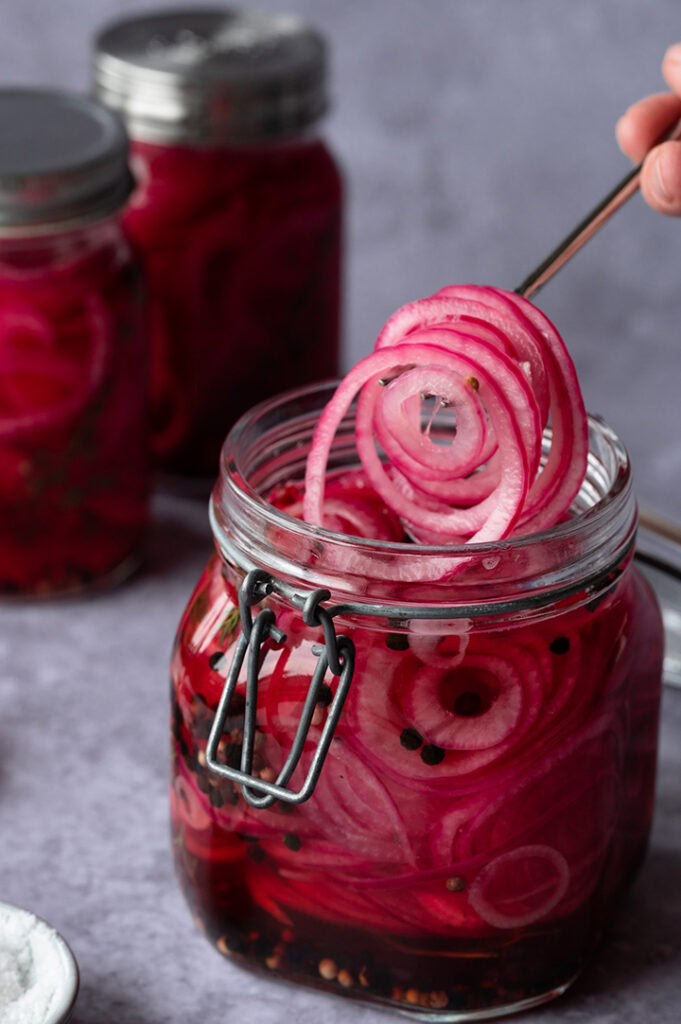 Eine Person nimmt eingelegte rote Zwiebeln mit einer Gabel aus dem Glas.