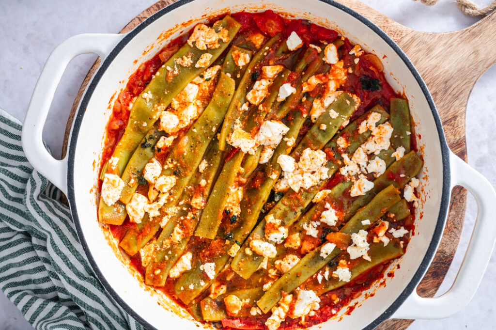 In einer Pfanne sind breite, grüne Bohnen in einer Tomatensauce.