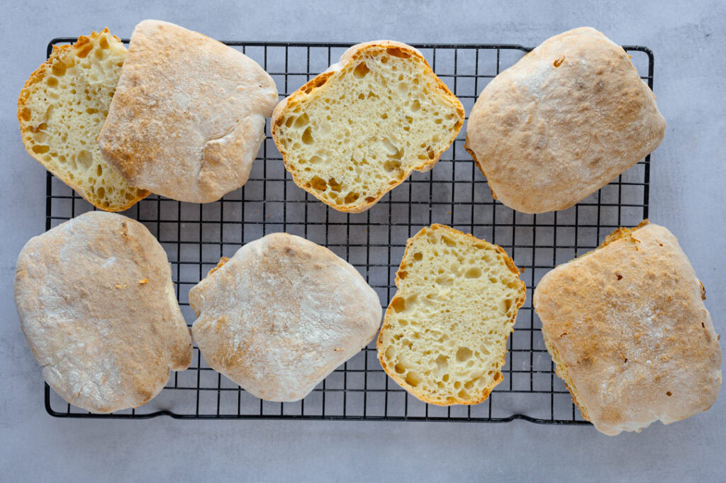 Sechs Ciabatta Brötchen liegen auf einem Gitter zum Auskühlen.
