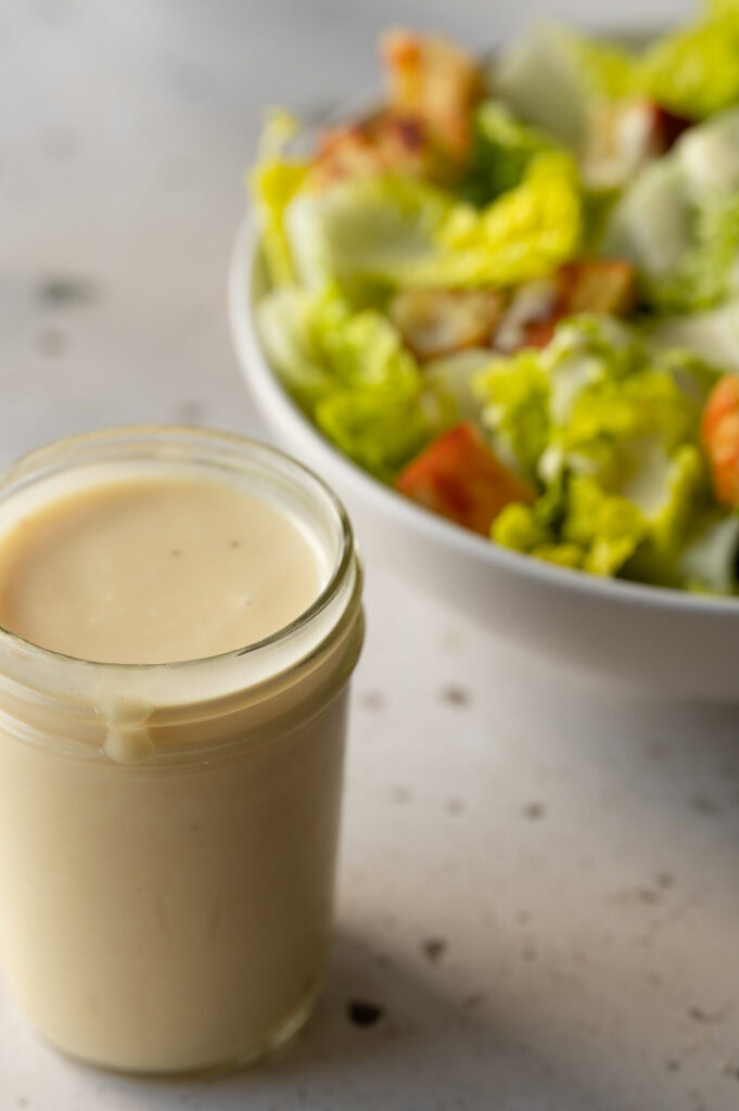 Ein Salat und ein Gefäß mit dem Dressing stehen auf dem Tisch.