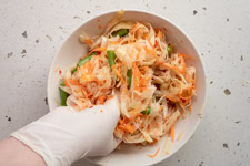 Eine Person knetet den Salat mit den Händen.