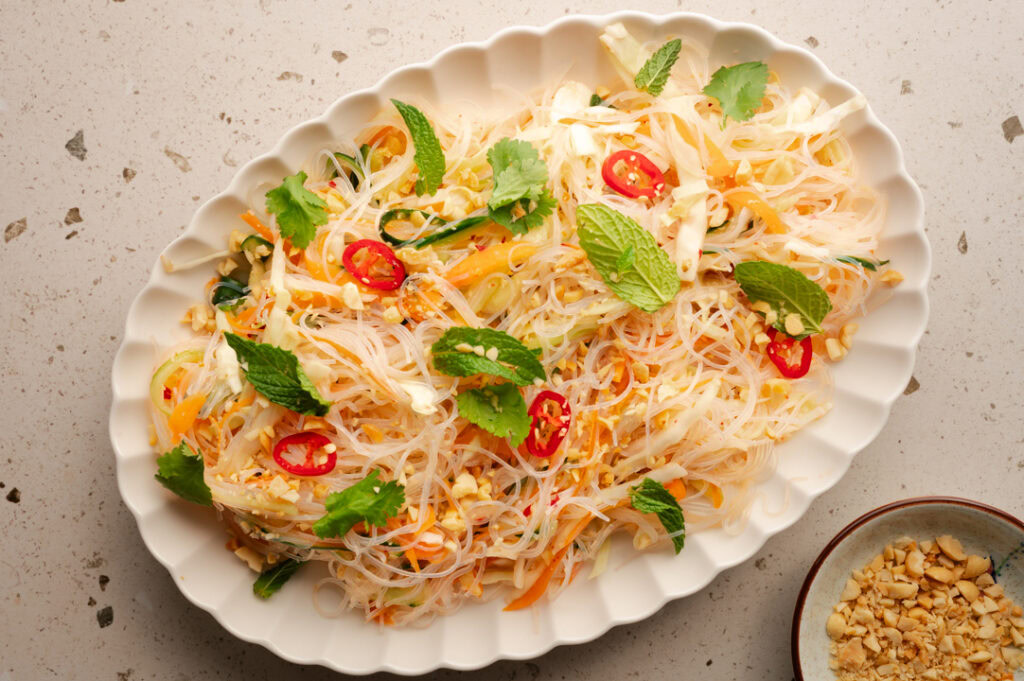 Eine Servierplatte mit asiatischem Glasnudelsalat steht auf einem Tisch.