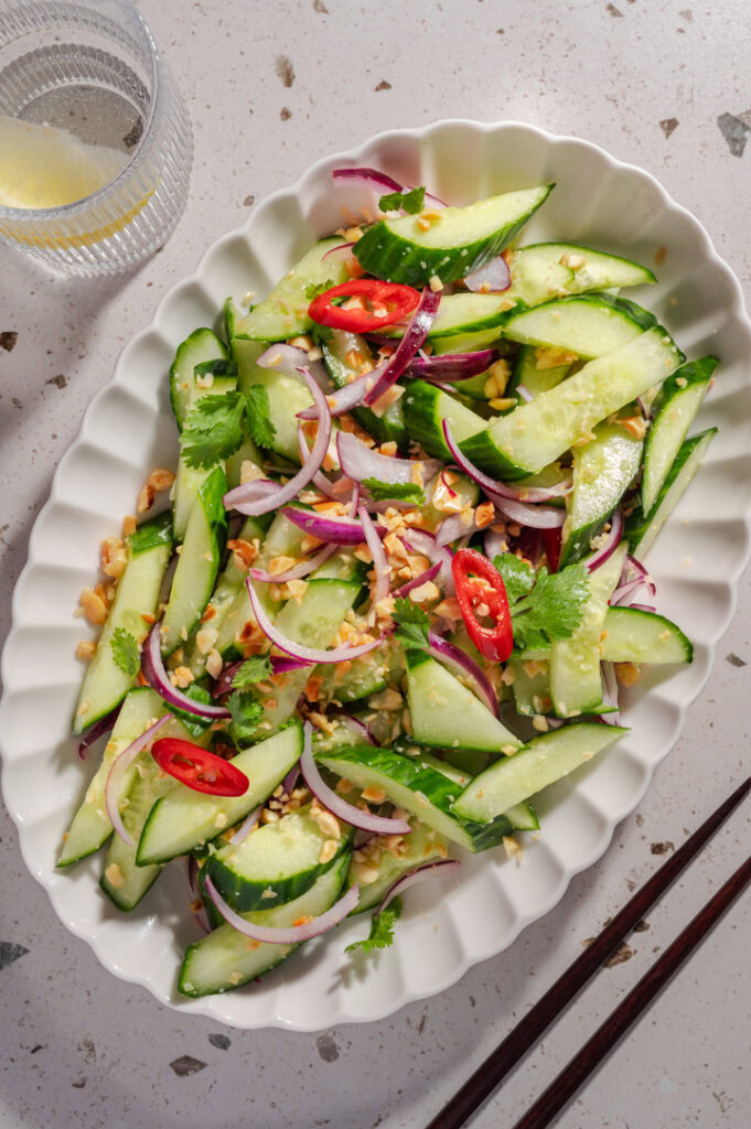 Eine Portion Thai Gurken-Salat neben einem Wasserglas und Stäbchen.