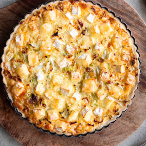 Eine Quiche mit Wirsing und Camembert steht auf einem Brett.