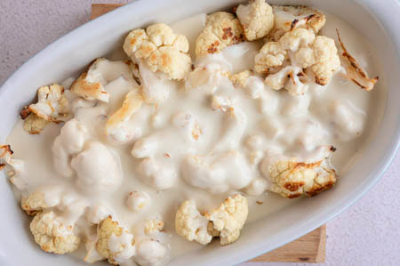 Der Blumenkohl ist in einer Auflaufform und wird mit Bechalsauce übergossen.