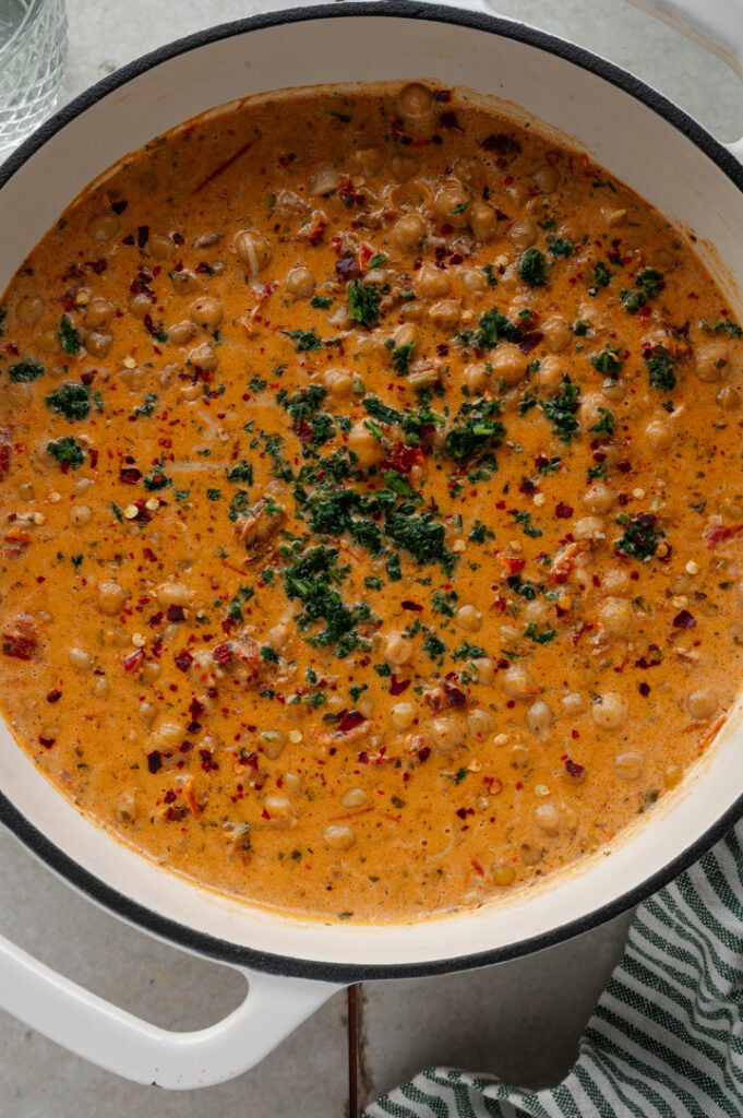 Die Pfanne mit Kichererbsen und mediterraner Sahnesauce steht auf einem Tisch.