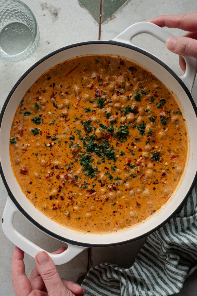 Eine Person stellt eine Pfanne mit cremigen Kichererbsen auf den Tisch.