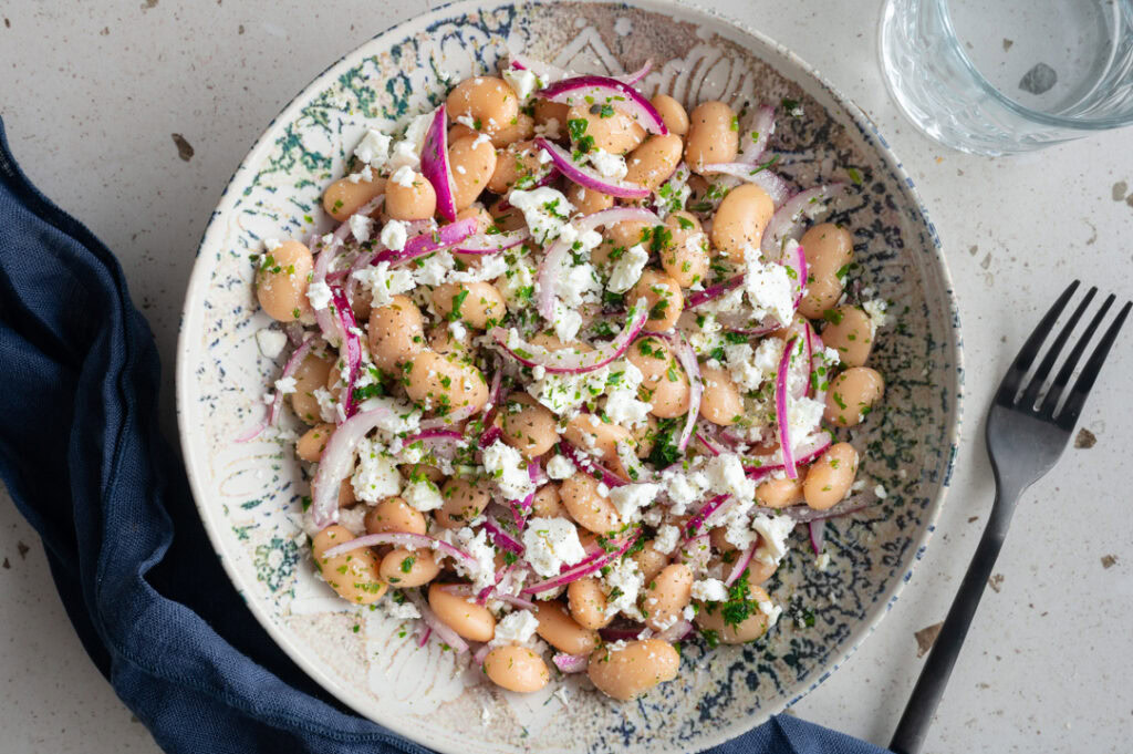 Ein Teller mit weißen Bohnen Salat und Feta steht auf dem Tisch.
