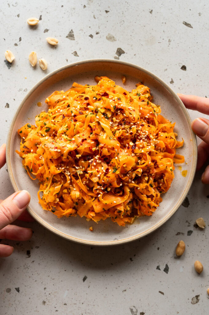 Eine Person stellt einen Teller mit asiatischem Karottensalat auf den Tisch.