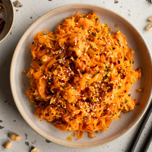 Ein Teller mit asiatischem Karottensalat und eine kleine Schale Chiliflocken stehen auf dem Tisch.