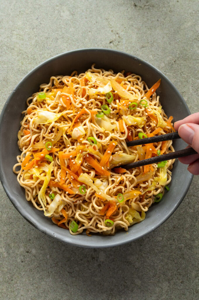 Eine Person isst Mie Nudeln mit Gemüse mit Stäbchen.