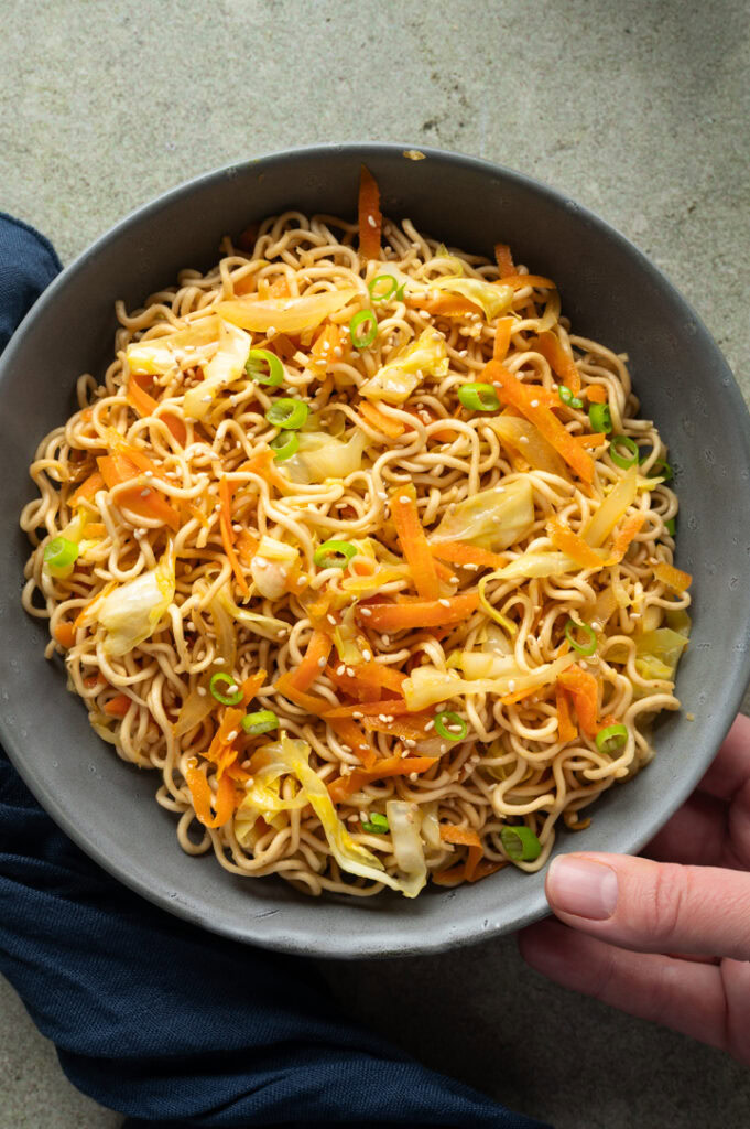 Eine Person stellt eine Schüssel der chinesischen, gebratenen Mie Nudeln auf den Tisch.