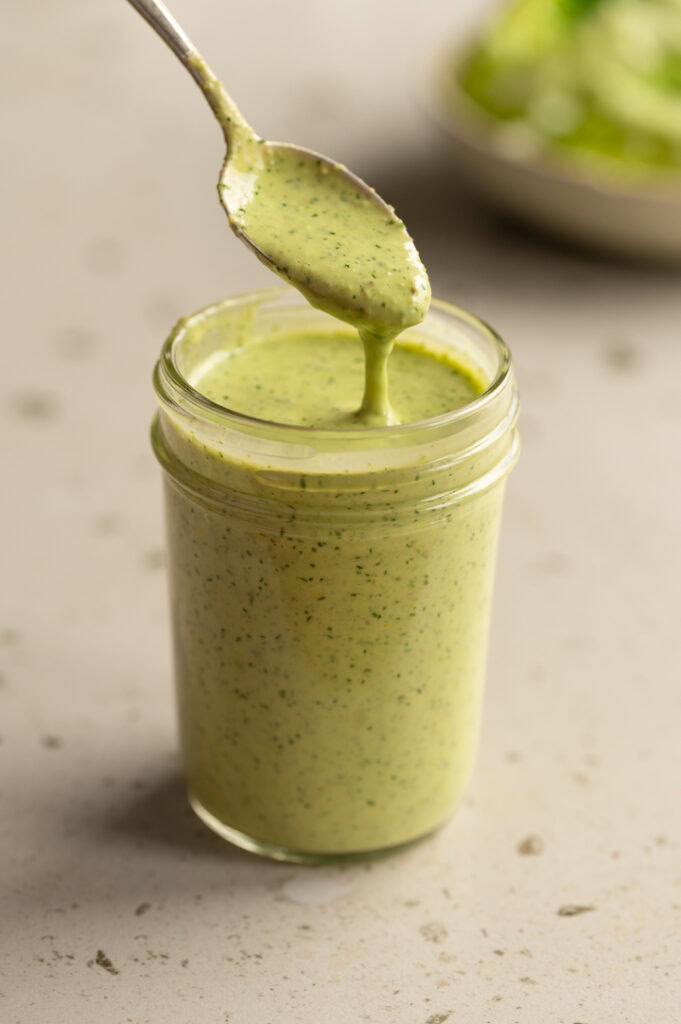 Eine Person nimmt mit einem Löffel Dill Dressing aus einem Glas.