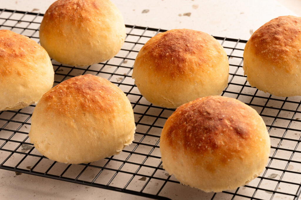 Ein Abkühlgitter mit 6 Kartoffelbrötchen, die darauf abkühlen.