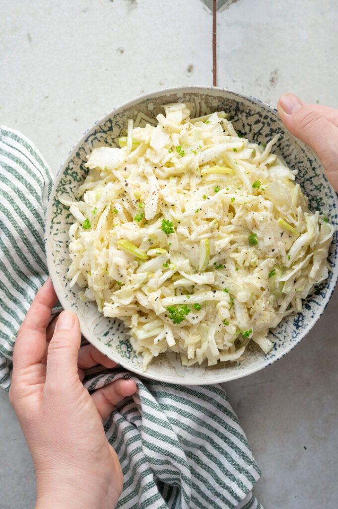 Eine Frau stellt eine Schüssel mit Krautsalat mit Apfel auf einen Tisch.