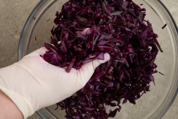 Der in feine Streifen geschnittene Rotkohl wird mit den Händen in einer Schüssel geknetet.