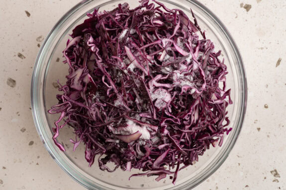 Der fein gehobelte Rotkohl wird mit Salz und Zucker in eine Schüssel gegeben.