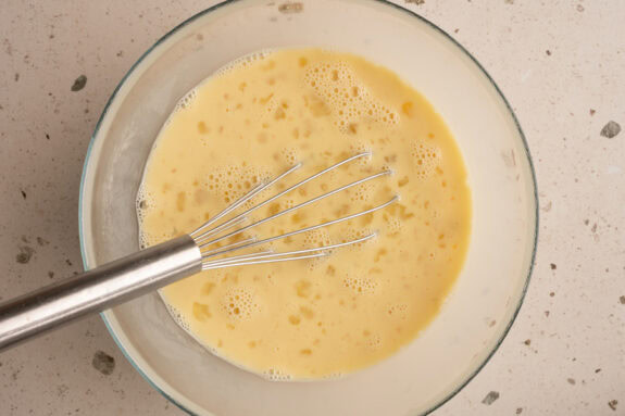 Milch und Eier werden in einer Schüssel mit einem Schneebesen verquirlt.