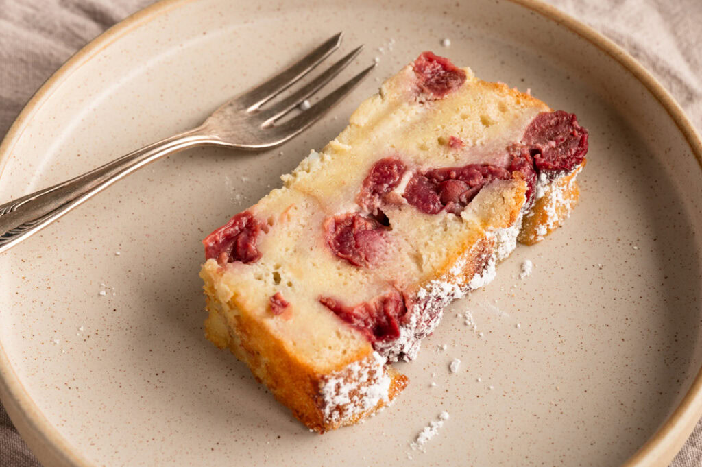 Ein Stück Armer Ritter Kuchen mit Kirschen liegt auf einem Teller.