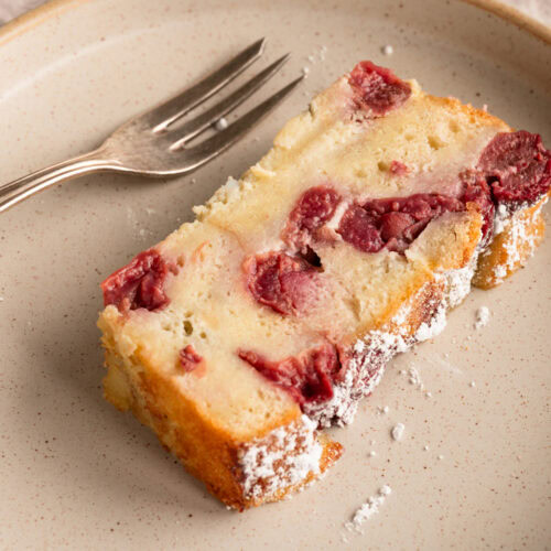 Ein Stück Armer Ritter Kuchen mit Kirschen liegt auf einem Teller.